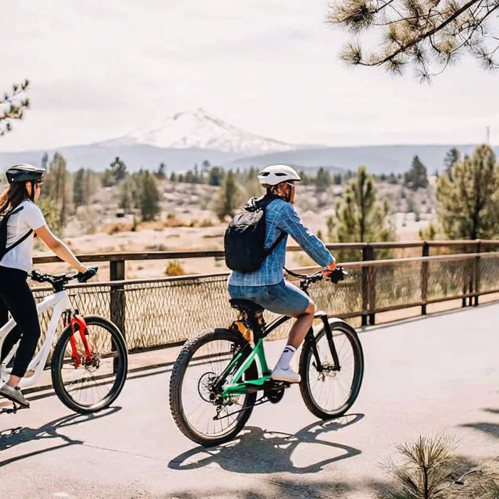Two cyclists riding electric bikes along the Deschutes River Trail in Bend, Oregon on a sunny day with Cascade Mountains in the background