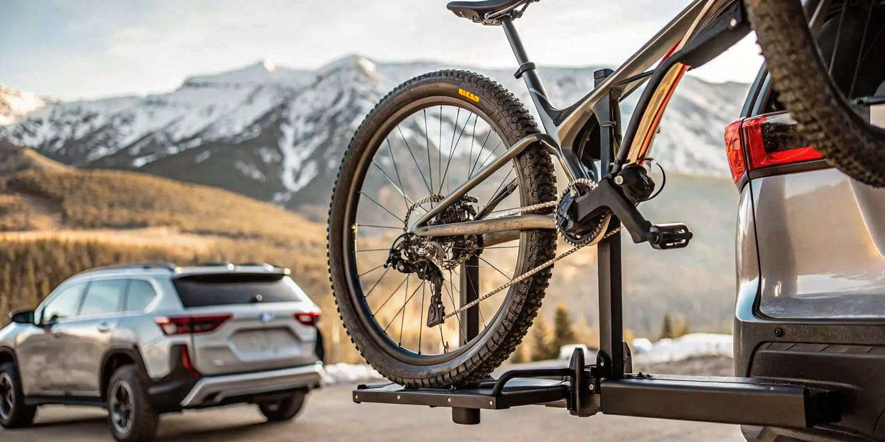 Heavy electric bike secured on a hitch-mounted platform car rack attached to an SUV with mountains in background