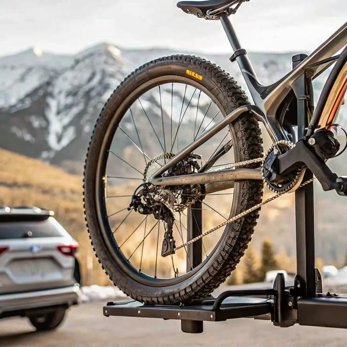 Heavy electric bike secured on a hitch-mounted platform car rack attached to an SUV with mountains in background
