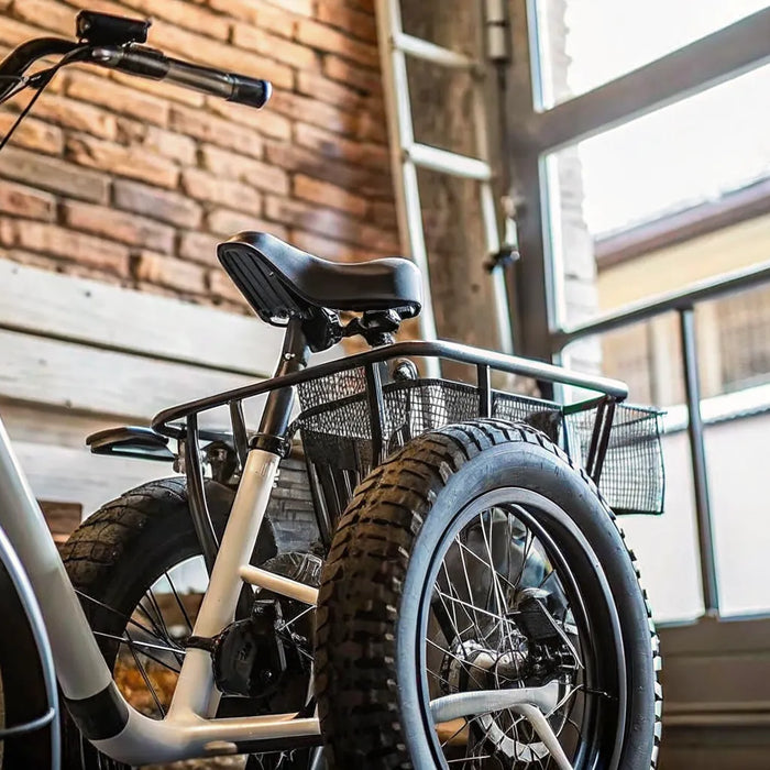 A folding fat tire electric trike with a rear cargo basket parked inside a garage.