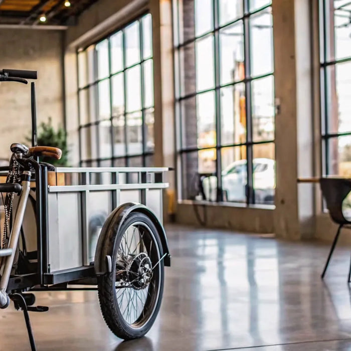 A modern electric tricycle for sale with a cargo basket on display in a showroom.