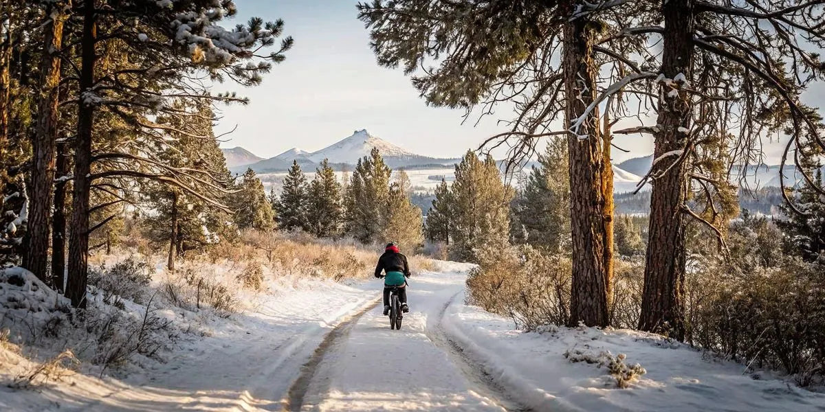 Person riding an electric bike on a snowy winter trail in Central Oregon with snow-covered pine trees and mountains