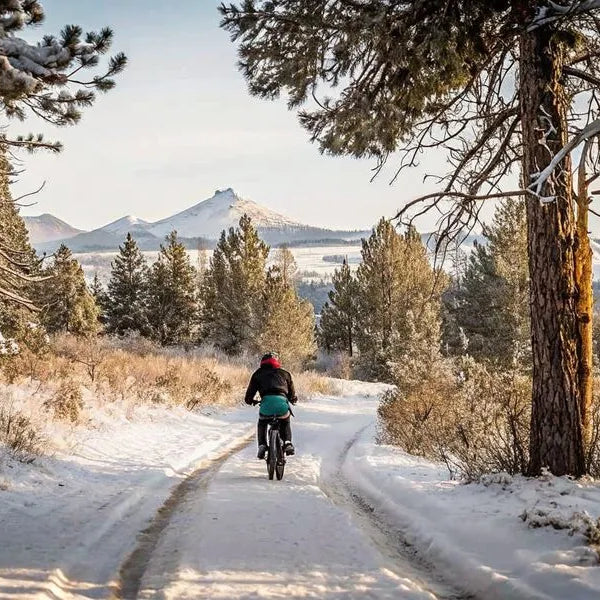 Person riding an electric bike on a snowy winter trail in Central Oregon with snow-covered pine trees and mountains